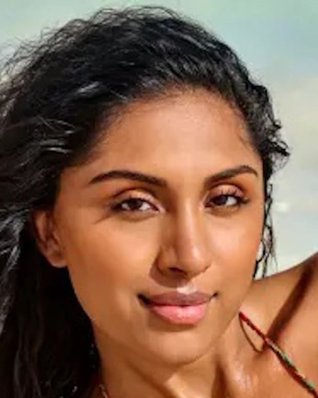 Manju lays on the beach in front of the ocean in a string bikini.